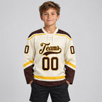 Custom Cream Lace Neck Hockey Jersey with Brown and Gold Lettering youth size worn by child model